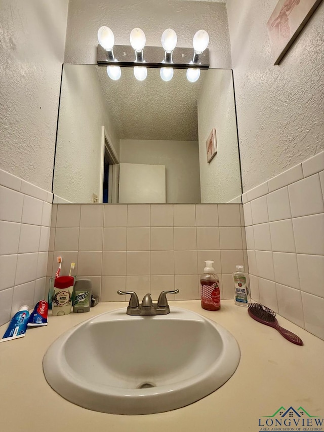 bathroom featuring sink, a textured ceiling, and tile walls