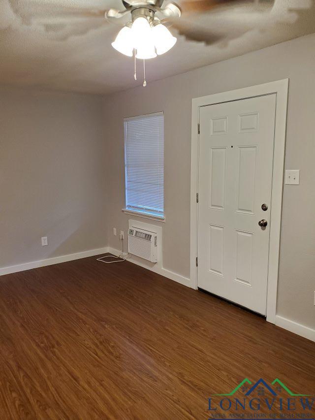 interior space featuring dark hardwood / wood-style flooring, a wall unit AC, and ceiling fan