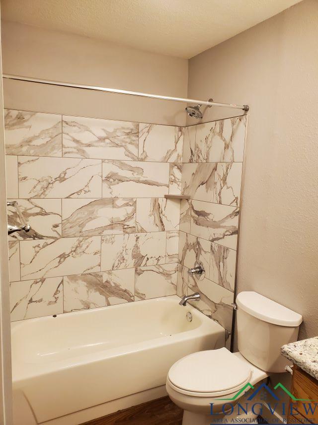 full bathroom with a textured ceiling, vanity, toilet, and tiled shower / bath