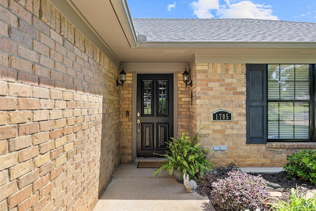 view of exterior entry featuring a shingled roof and brick siding