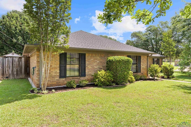 ranch-style house featuring a front yard, brick siding, roof with shingles, and fence