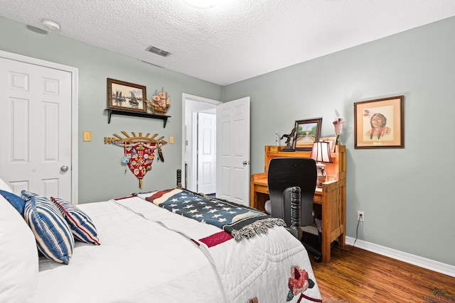 bedroom with a textured ceiling, baseboards, visible vents, and wood finished floors