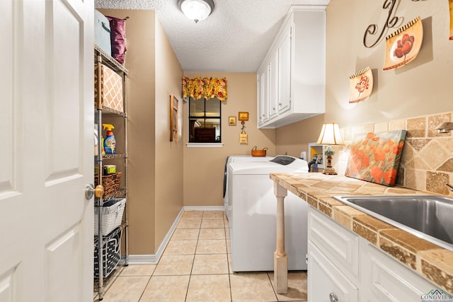 laundry room featuring light tile patterned floors, a sink, cabinet space, a textured ceiling, and washer and clothes dryer