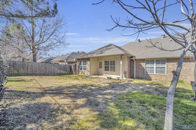 rear view of property featuring roof with shingles, brick siding, fence, and a lawn