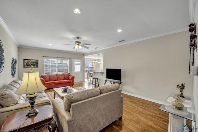 living area featuring baseboards, visible vents, a ceiling fan, ornamental molding, and wood finished floors