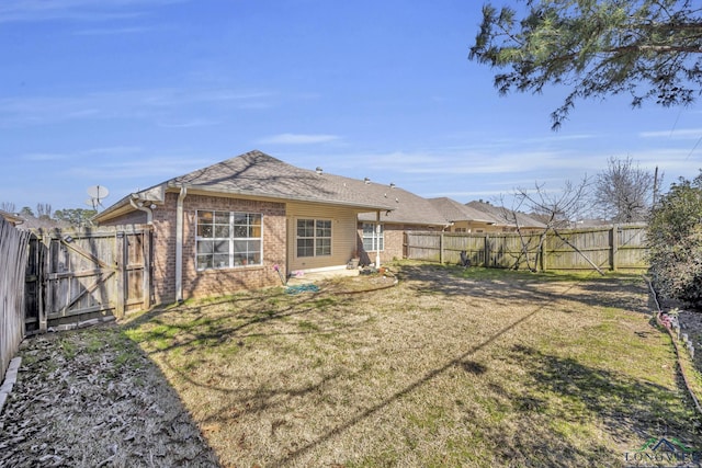 rear view of property featuring a gate, brick siding, a lawn, and a fenced backyard