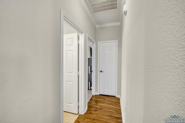 corridor with a textured wall, visible vents, crown molding, and wood finished floors