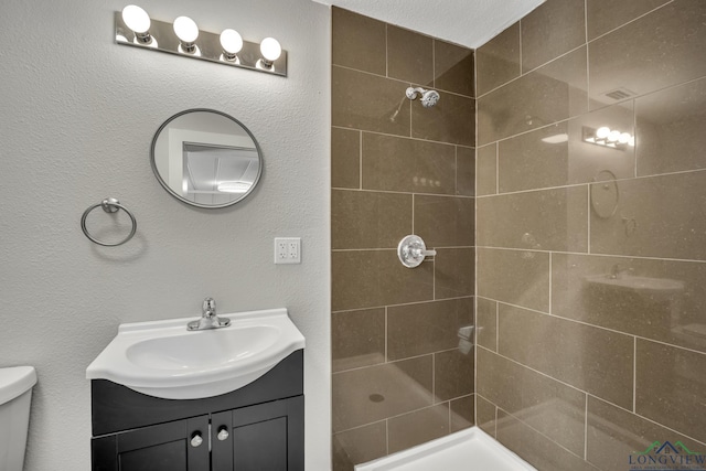 bathroom with vanity, toilet, and tiled shower