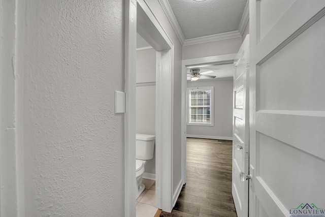 hallway featuring wood-type flooring, ornamental molding, and a textured ceiling