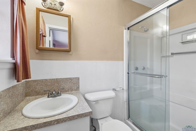 bathroom featuring a wainscoted wall, toilet, vanity, and a stall shower