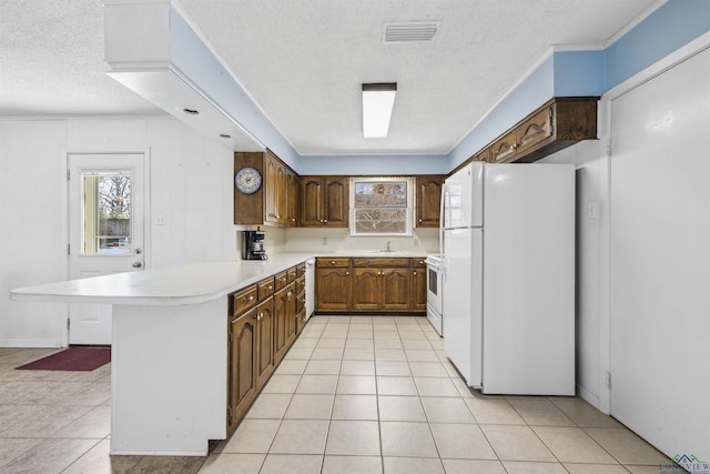 kitchen featuring light countertops, light tile patterned floors, a peninsula, white appliances, and a sink