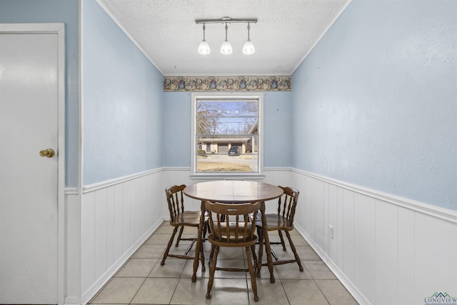 tiled dining area featuring a textured ceiling, ornamental molding, and wainscoting