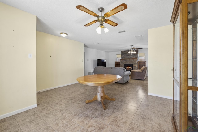 living area featuring baseboards, visible vents, ceiling fan, a stone fireplace, and a textured ceiling