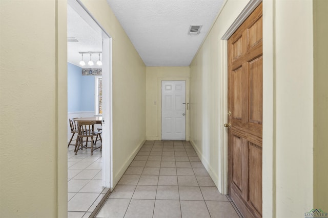 corridor featuring visible vents, baseboards, light tile patterned floors, rail lighting, and a textured ceiling