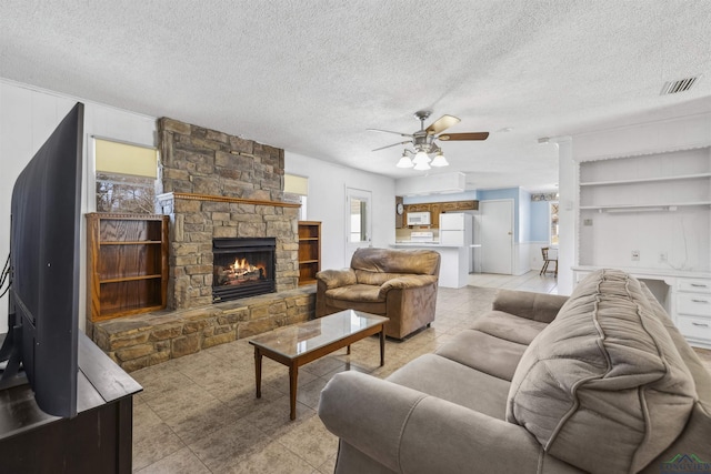 living room with a stone fireplace, visible vents, and a textured ceiling