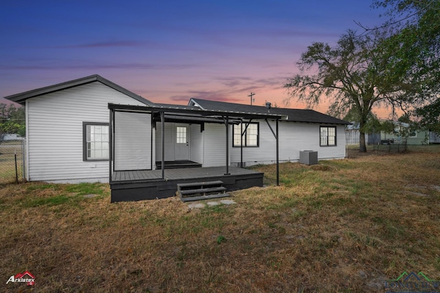 back house at dusk with a lawn, cooling unit, and a wooden deck