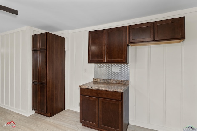 kitchen with dark brown cabinetry, light hardwood / wood-style floors, light stone counters, and backsplash