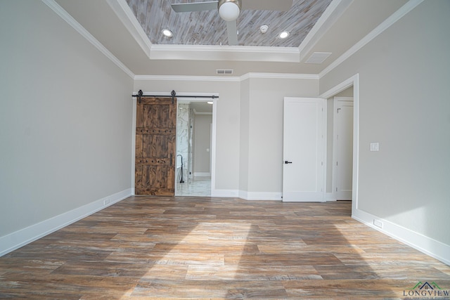 empty room featuring a raised ceiling, crown molding, a barn door, and dark hardwood / wood-style flooring