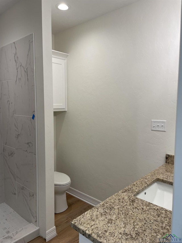 bathroom featuring vanity, toilet, wood-type flooring, and tiled shower