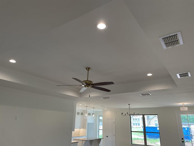 interior details featuring a tray ceiling, backsplash, ceiling fan with notable chandelier, and ornamental molding