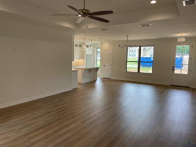 unfurnished living room with ceiling fan with notable chandelier, dark hardwood / wood-style floors, and a tray ceiling