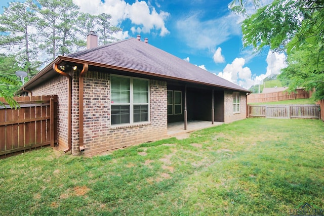 back of house with brick siding, a fenced backyard, a chimney, a lawn, and a patio