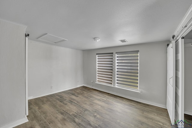 585 Naples Dr, Omaha, TX 75571 - unfurnished bedroom with a textured ceiling, visible vents, a barn door, and wood finished floors