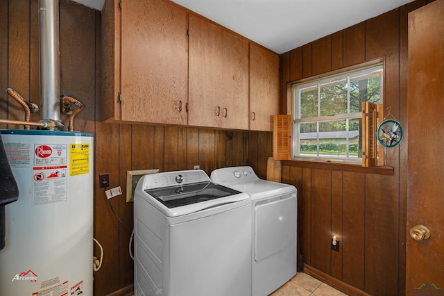 laundry area with cabinets, gas water heater, wooden walls, washing machine and dryer, and light tile patterned flooring