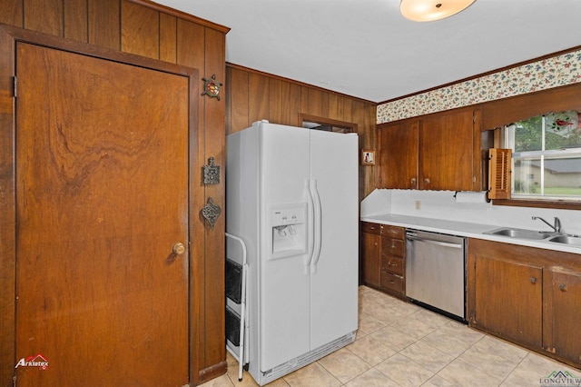 kitchen with wooden walls, sink, white refrigerator with ice dispenser, light tile patterned floors, and dishwasher