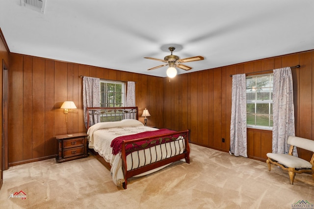 carpeted bedroom featuring multiple windows, ceiling fan, and wooden walls