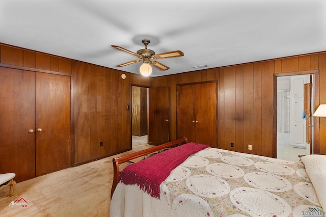 carpeted bedroom featuring wood walls, ensuite bathroom, ceiling fan, and multiple closets