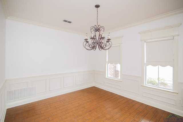 spare room featuring wood-type flooring, crown molding, and a notable chandelier