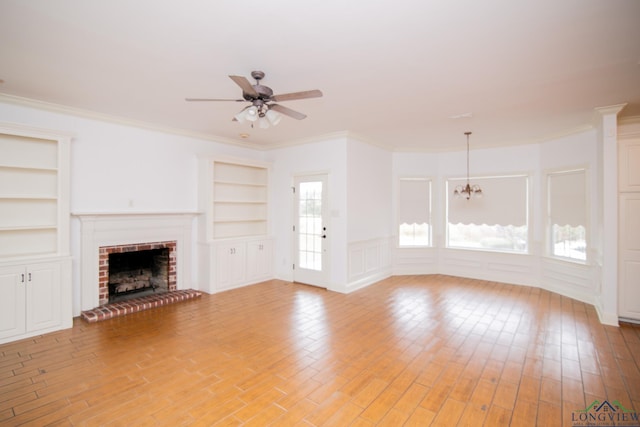 unfurnished living room with ceiling fan with notable chandelier, crown molding, light hardwood / wood-style flooring, built in features, and a fireplace