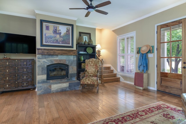 living room with hardwood / wood-style floors, ceiling fan, a stone fireplace, and ornamental molding