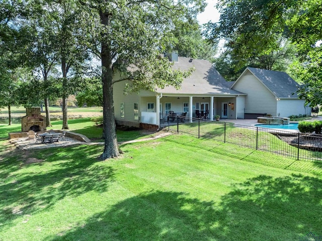 rear view of property with a lawn, an outdoor stone fireplace, and a patio area