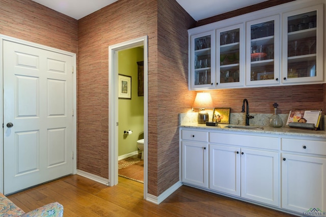 bar with white cabinets, light hardwood / wood-style floors, light stone counters, and sink