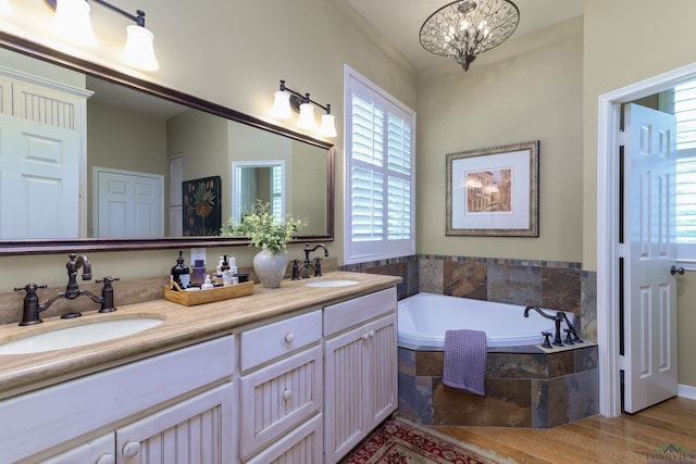 bathroom featuring vanity, wood-type flooring, tiled tub, and a chandelier