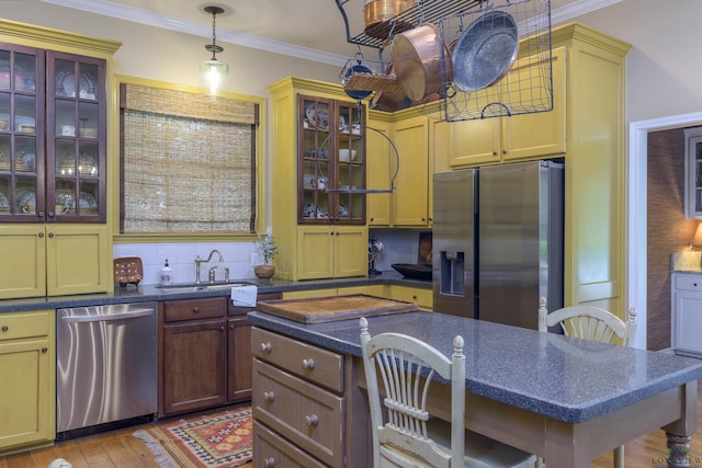 kitchen with sink, pendant lighting, light wood-type flooring, appliances with stainless steel finishes, and ornamental molding