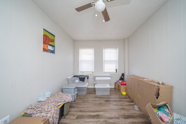 interior space featuring a textured ceiling, light hardwood / wood-style floors, ceiling fan, and wood walls