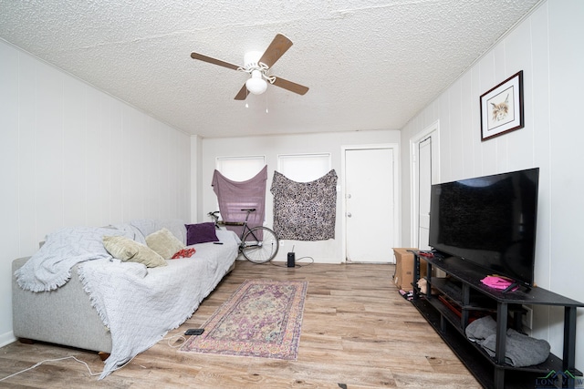 living room with ceiling fan, light hardwood / wood-style flooring, a textured ceiling, and wooden walls