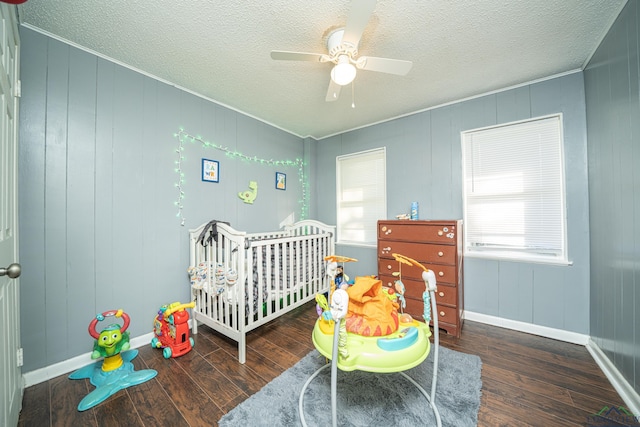 bedroom with multiple windows, a nursery area, ceiling fan, and dark wood-type flooring