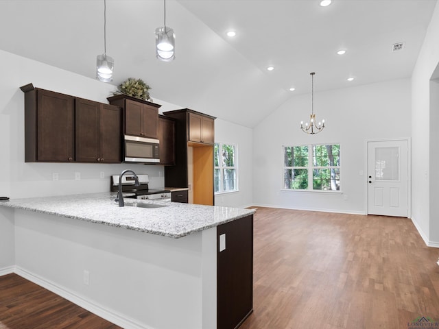 kitchen featuring dark brown cabinetry, light stone countertops, stainless steel appliances, kitchen peninsula, and decorative light fixtures