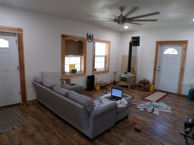 living room with a wood stove, ceiling fan, baseboards, and wood finished floors