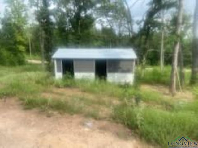 view of outdoor structure with dirt driveway, a carport, and an outbuilding