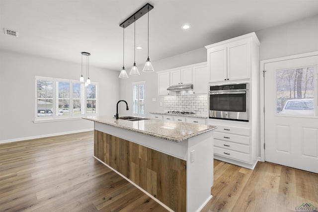 kitchen featuring visible vents, under cabinet range hood, decorative backsplash, stainless steel appliances, and a sink