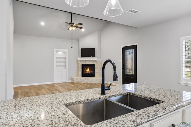 kitchen with visible vents, lofted ceiling, a sink, a stone fireplace, and light stone countertops