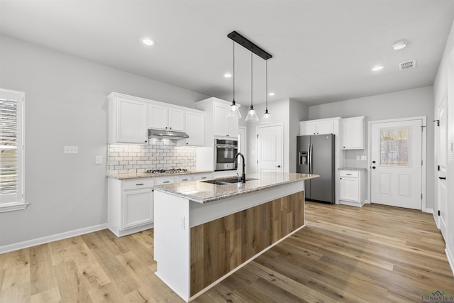 kitchen with tasteful backsplash, under cabinet range hood, appliances with stainless steel finishes, white cabinetry, and a sink