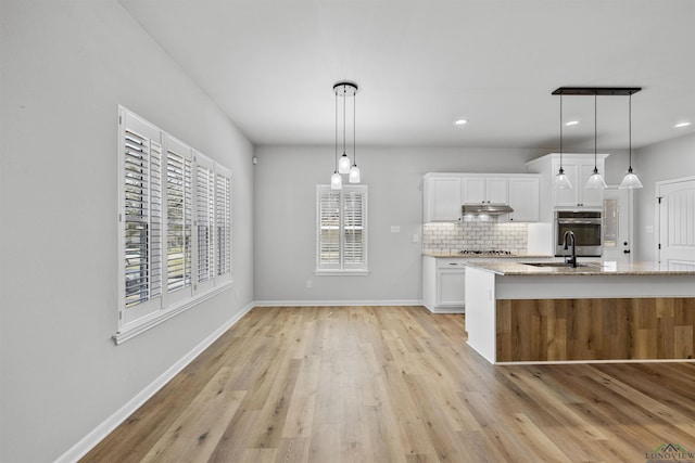 kitchen featuring backsplash, under cabinet range hood, white cabinets, stainless steel appliances, and a sink