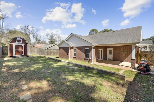 rear view of house with brick siding, a storage shed, a fenced backyard, a patio area, and an outbuilding