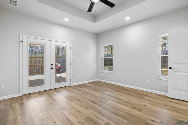 empty room featuring visible vents, light wood-type flooring, recessed lighting, french doors, and a raised ceiling